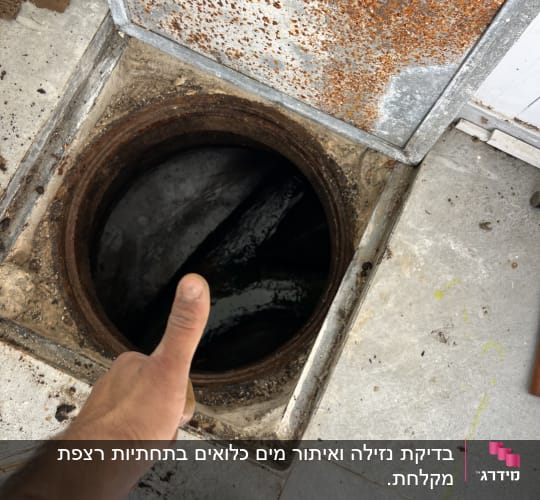 אדם מצביע על פתח ביוב פתוח עם מכסה חלוד